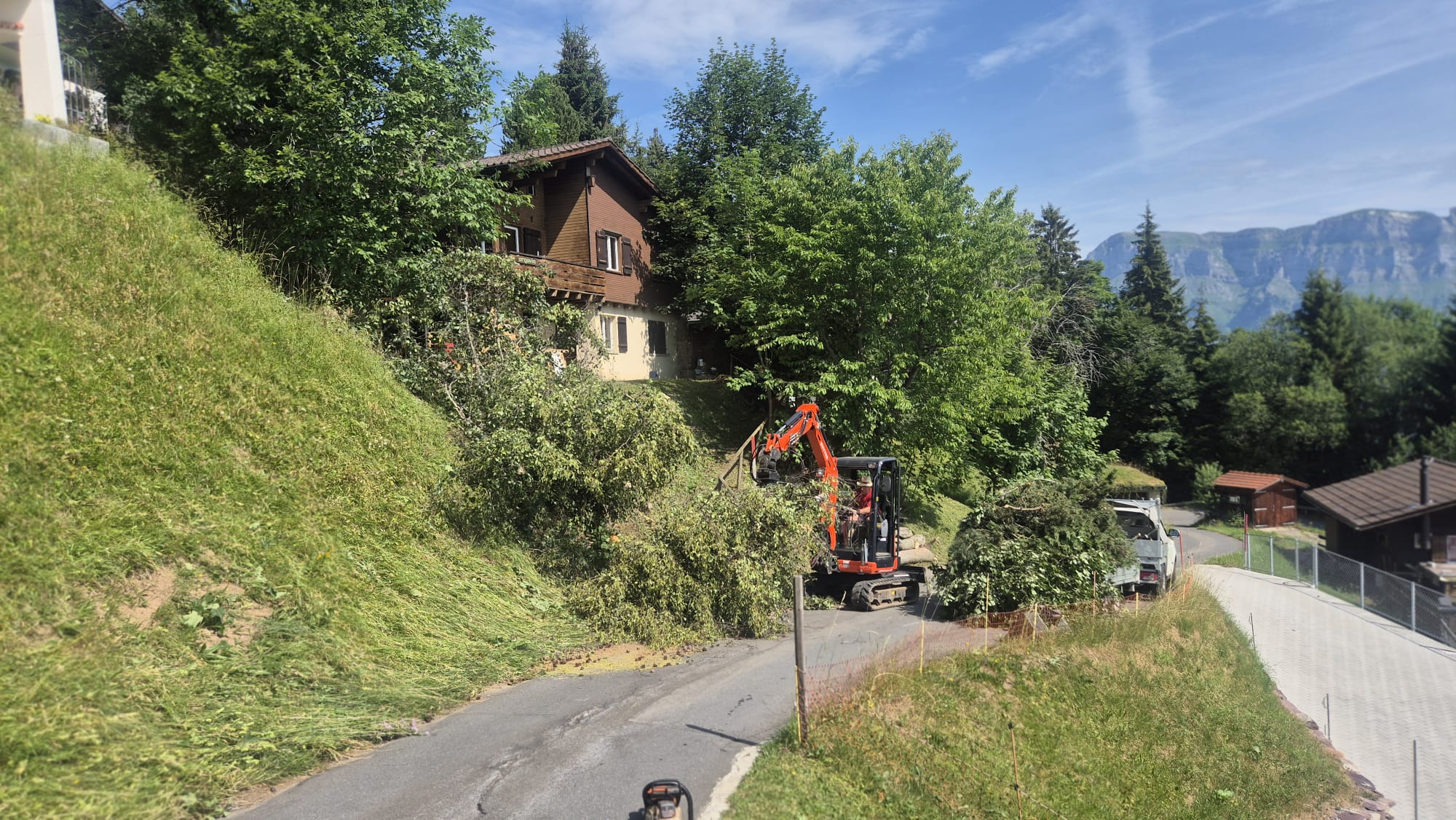 Graafmachine ruimt begroeiing op de helling naast het chalet